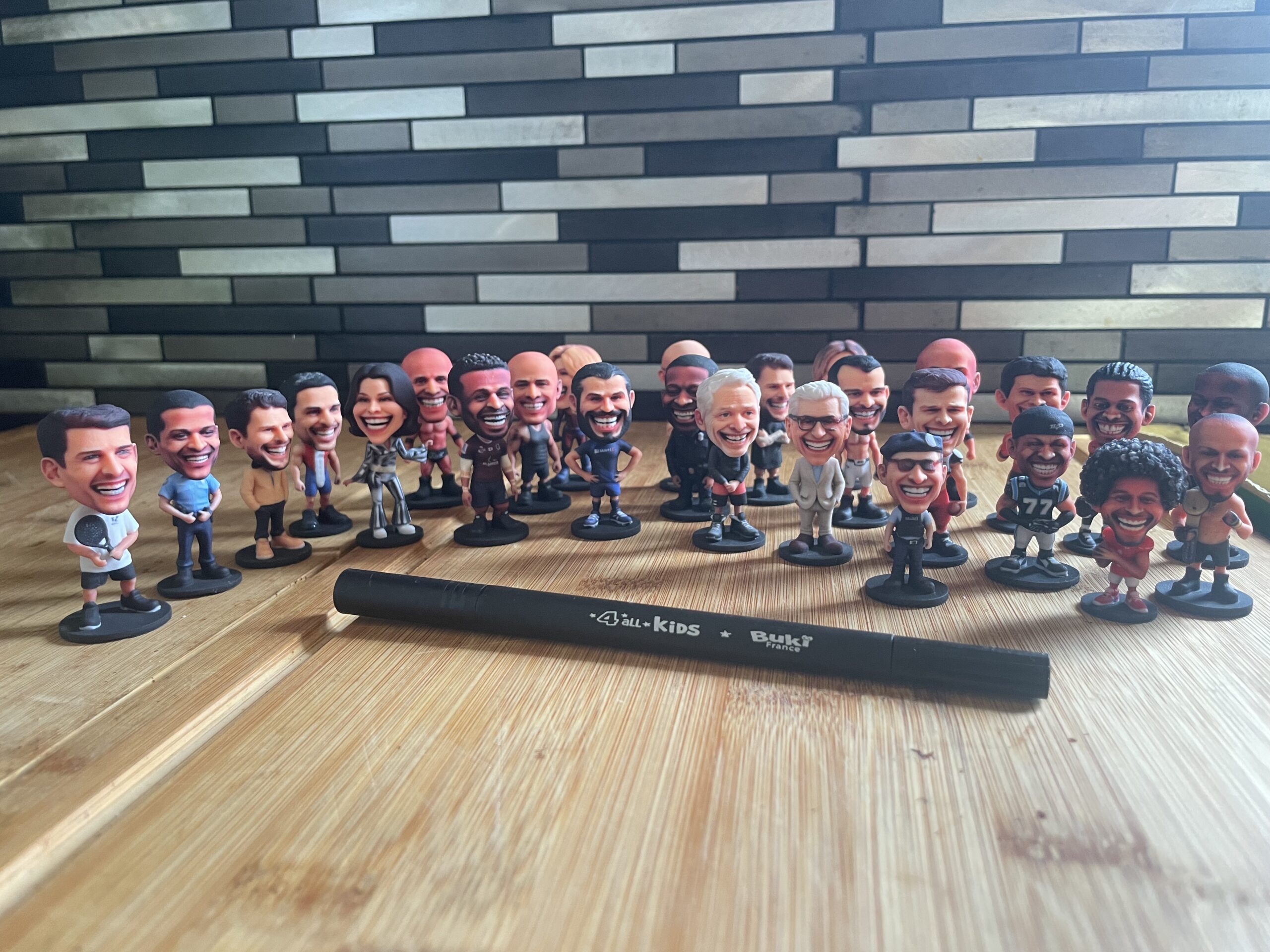 A large batch of custom bobblehead figurines lined up, with a pen in front for scale